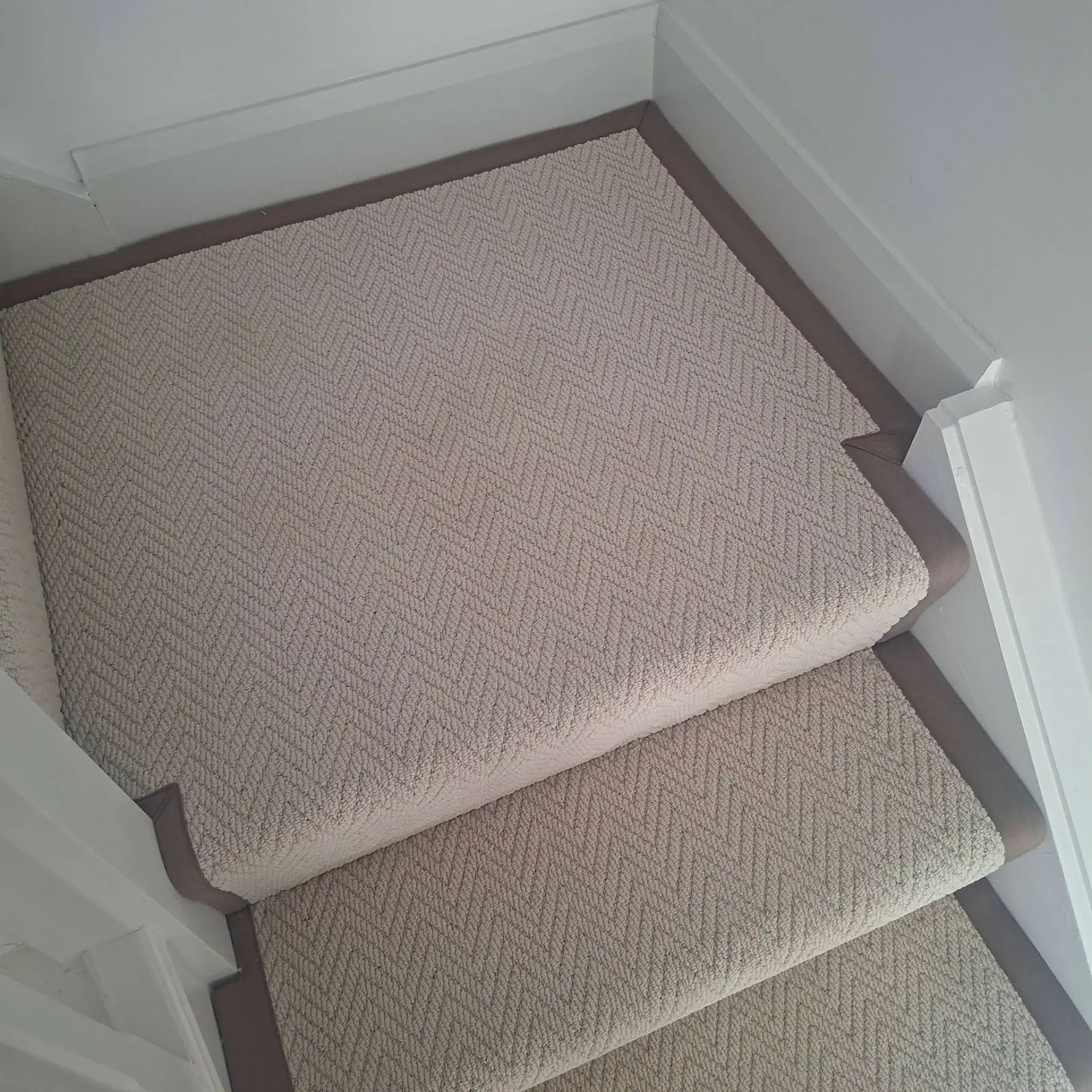 Close-up of a beige herringbone stair runner with taupe binding