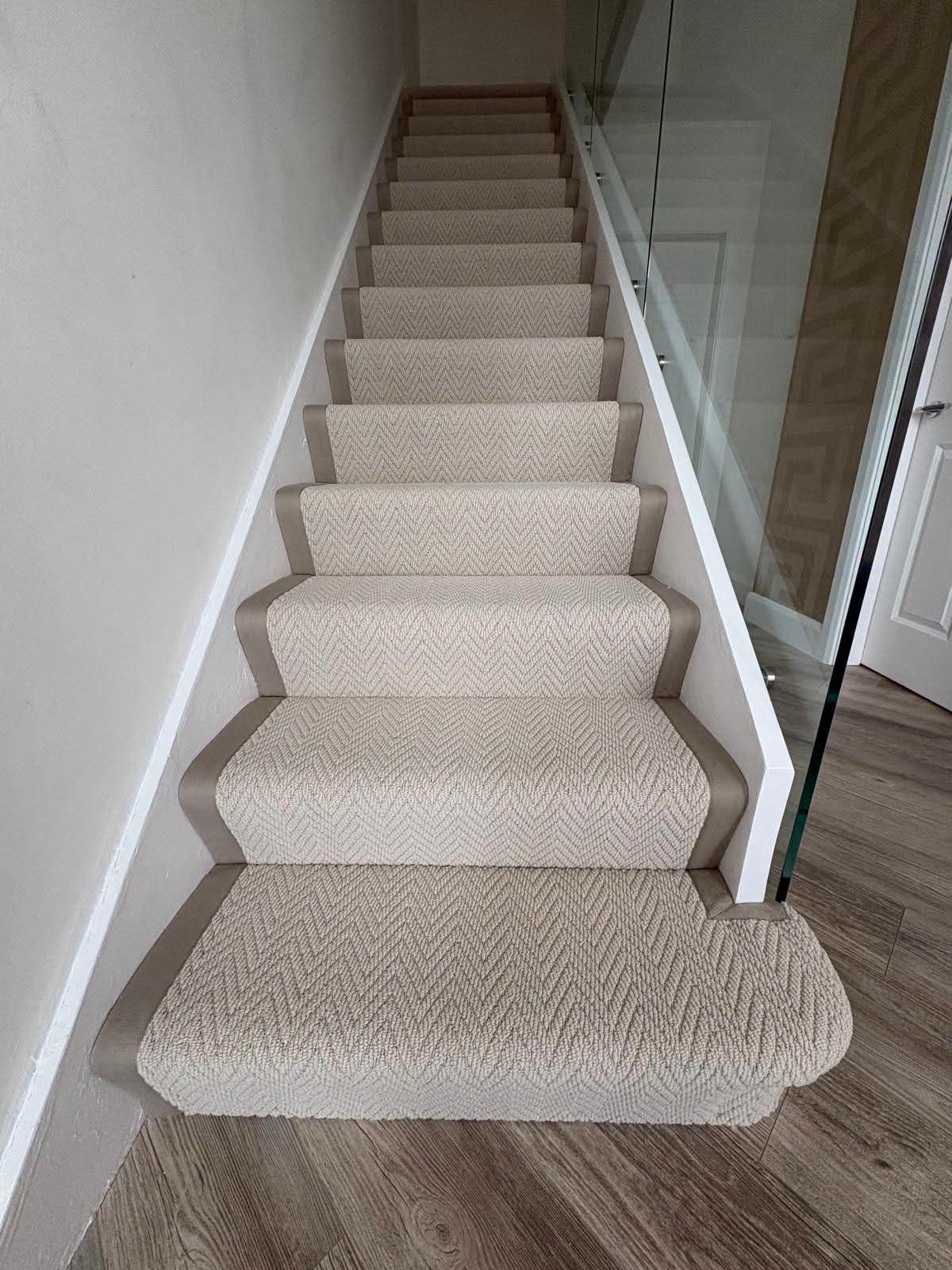 Full staircase fitted with a beige herringbone runner and taupe binding