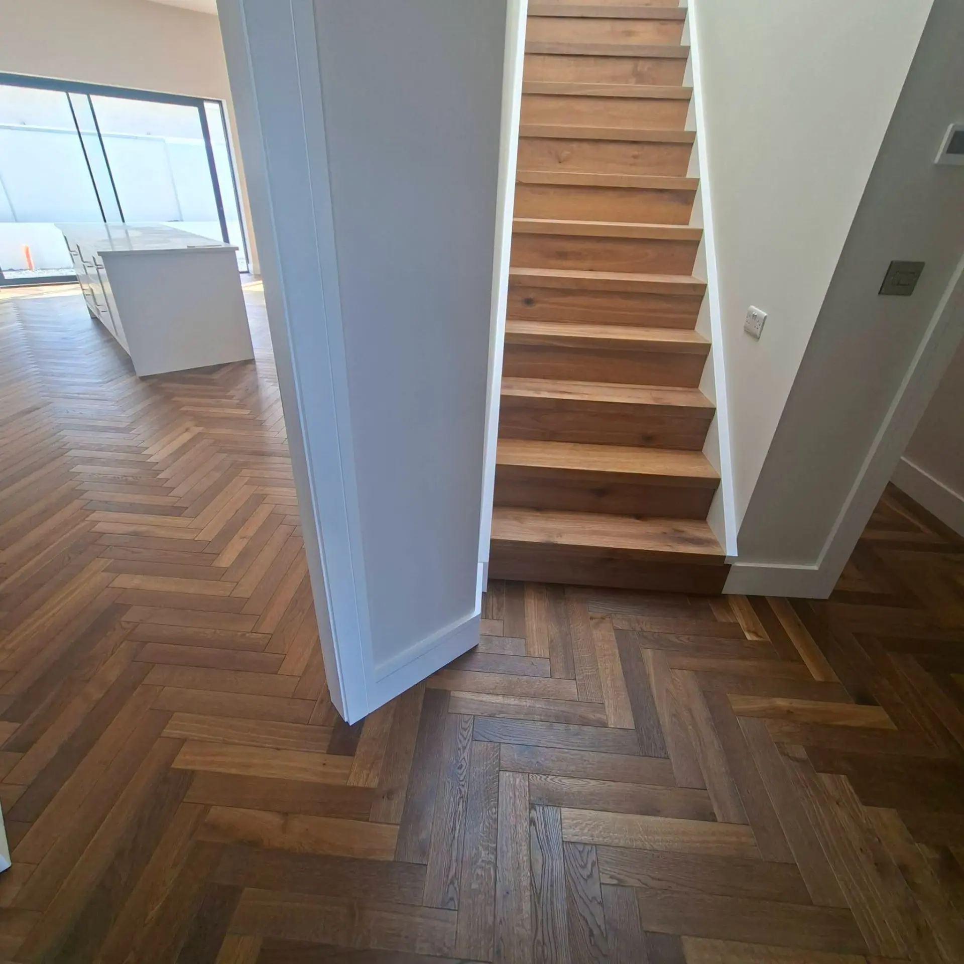 Bespoke oak stair system flowing into a herringbone hallway floor
