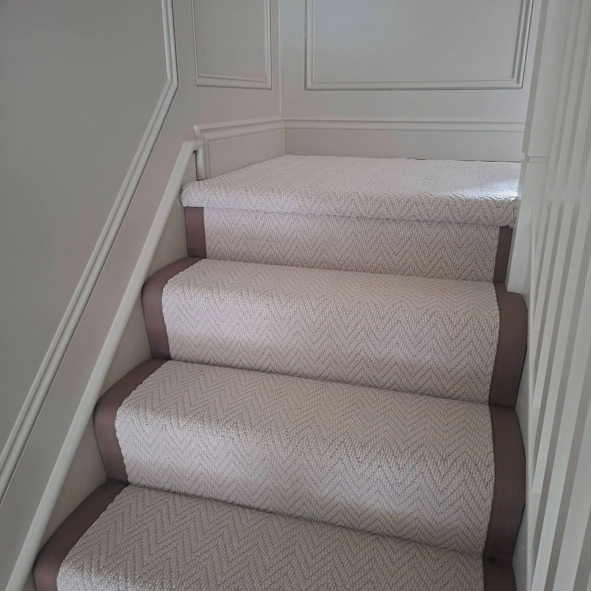 Beige herringbone stair runner with taupe binding on white stairs